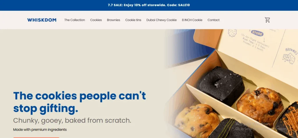 Screenshot of the Whiskdom website homepage. A top blue promotional bar reads "7.7 SALE: Enjoy 10% off storewide. Code: SALE10." Below it, the navigation bar displays the "Whiskdom" logo alongside links for "The Collection," "Cookies," "Brownies," "Cookie tins," "Dubai Chewy Cookie," "8 INCH Cookie," "Contact," and a shopping cart icon. The main section features the large text "The cookies people can't stop gifting. Chunky, gooey, baked from scratch. Made with premium ingredients," next to an image of an open bakery box filled with assorted thick cookies and brownies.