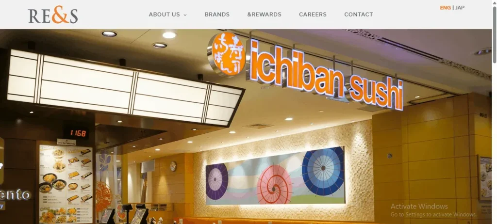 A website screenshot featuring the storefront of an Ichiban Sushi restaurant under a corporate header for RE&S. The restaurant storefront displays a bright, glowing orange and white "ichiban sushi" sign above a textured wall decorated with a colorful Japanese parasol art panel. A menu board is visible on the left, and a Windows activation watermark appears in the bottom right corner.