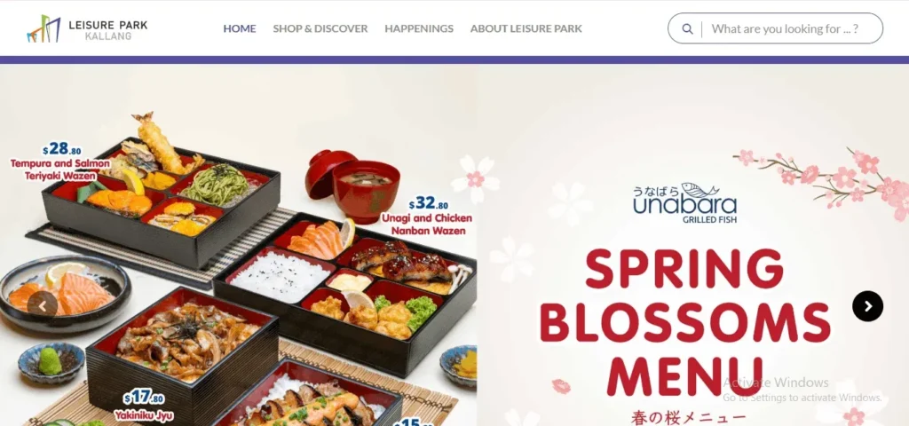 Screenshot of a website header for "Leisure Park Kallang" featuring a promotional banner for "Unabara Grilled Fish." The white top navigation bar includes the mall logo, search input, and menu links. Below, the main carousel banner showcases a Japanese "Spring Blossoms Menu" decorated with pink cherry blossoms. On the left side, several Japanese bento boxes and bowls are displayed with prices, including a Tempura and Salmon Teriyaki Wazen for $28.80, an Unagi and Chicken Nanban Wazen for $32.80, and a Yakiniku Jyu for $17.80. Navigation arrows flank the left and right edges of the banner image.