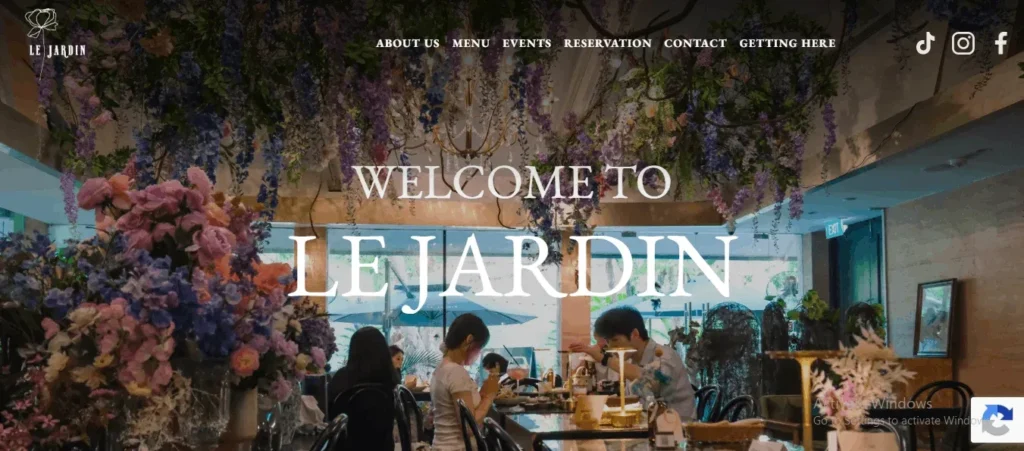 Website landing page for Le Jardin restaurant, featuring large overlay text reading "WELCOME TO LE JARDIN" over a busy, indoor dining room adorned with heavy floral ceiling arrangements.