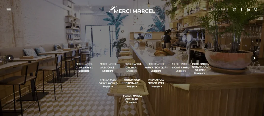 Homepage hero section of the Merci Marcel website featuring the interior design of a café with tropical wallpaper, potted plants, a long service counter with pastries, and geometric floor tiles. White text overlays list various locations across Singapore, including Club Street, East Coast, Orchard, Robertson Quay, Tiong Bahru, and Serangoon Garden.