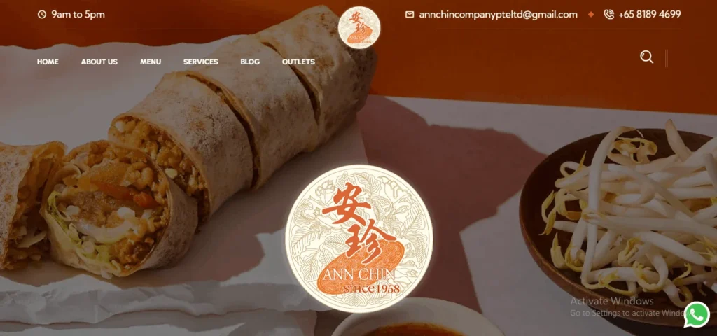 Website homepage header for "Ann Chin Popiah" featuring sliced popiah (fresh spring rolls) filled with turnip and vegetables alongside a side bowl of fresh bean sprouts. Centered on the page is a circular logo reading "Ann Chin since 1958" in traditional Chinese calligraphy and English, set against an orange and white background with top contact navigation controls.