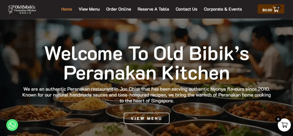 Homepage of Old Bibik’s Peranakan Kitchen, featuring a blurred background of Peranakan dishes with the headline “Welcome To Old Bibik’s Peranakan Kitchen,” a short restaurant description, a “View Menu” button, top navigation links, and WhatsApp and shopping cart icons.