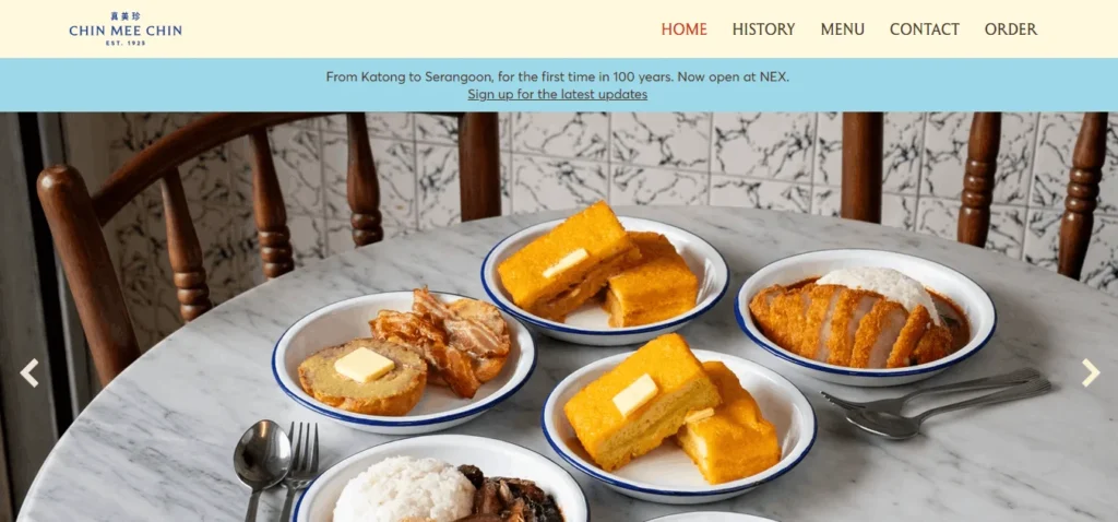 Chin Mee Chin homepage featuring a marble dining table with plates of traditional Singaporean breakfast foods, including kaya toast, buttered toast, fried eggs, luncheon meat, and rice dishes, with the restaurant logo and navigation menu at the top.