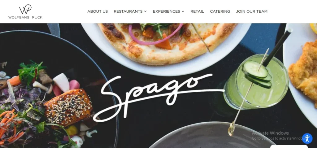 Wolfgang Puck Spago website header showing a flat-lay assortment of gourmet dishes, including a salmon salad, artisan pizza, chicken schnitzel, and a cucumber cocktail.