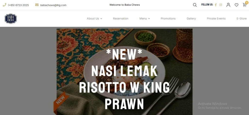 Screenshot of the Baba Chews homepage featuring a banner for a new dish called "Nasi Lemak Risotto w King Prawn." The dish shows blue pea flower rice risotto topped with a grilled king prawn, soft-boiled egg, and sambal, served alongside a fork and spoon on a patterned tablecloth.