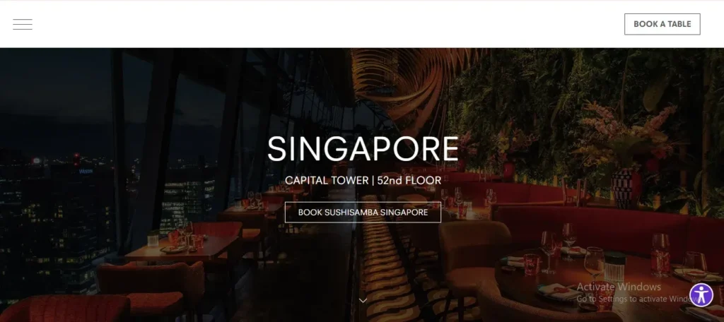 Screenshot of the web landing page for SUSHISAMBA Singapore. The header displays a hamburger menu on the top left and a "BOOK A TABLE" button on the top right. Overlaying a dim background image of a high-rise restaurant interior with plush red seating and night views of city skyscrapers, central text reads "SINGAPORE" and "CAPITAL TOWER | 52nd FLOOR," positioned above a button labeled "BOOK SUSHISAMBA SINGAPORE."