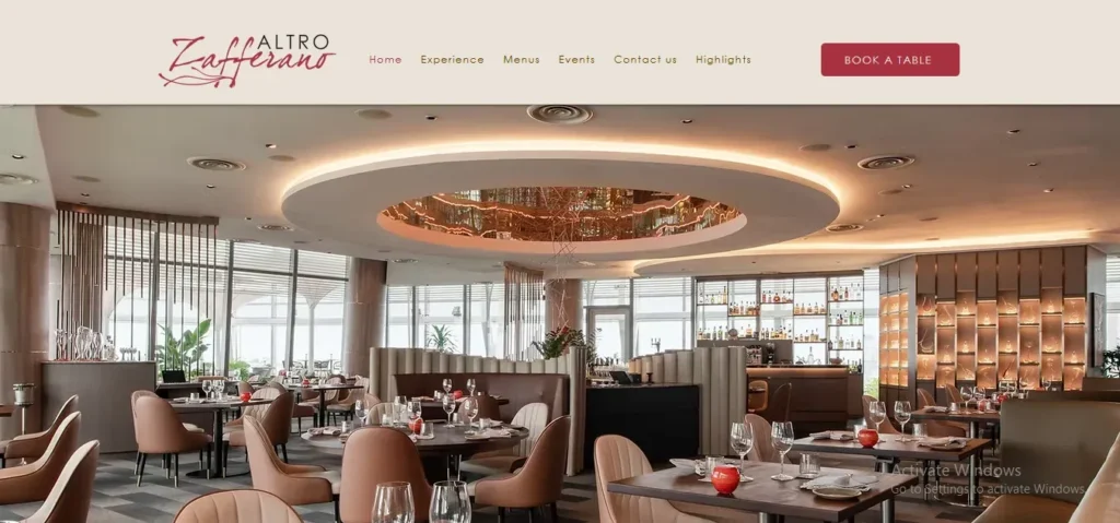 Screenshot of the Altro Zafferano website home page, featuring an elegant interior view of a fine-dining dining room with round tables, warm lighting, plush seating, and floor-to-ceiling glass windows.