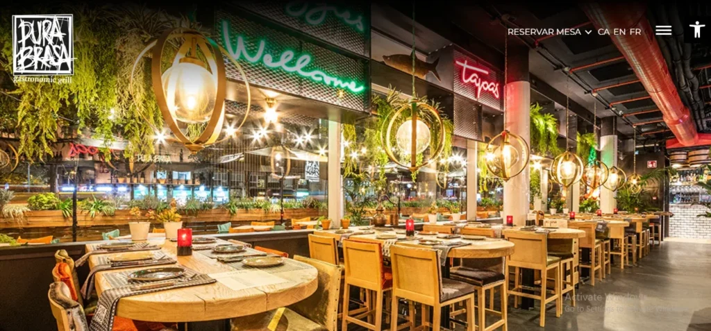 Website banner for Pura Brasa Gastronomic Grill showing a vibrant restaurant interior with wooden tables, spherical pendant lights, hanging greenery, and neon signage.