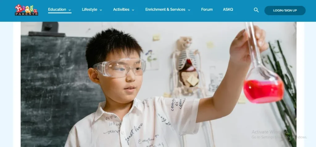Homepage header for KiasuParents featuring a young boy wearing safety goggles holding up a glass flask filled with red liquid during a science experiment.
